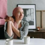 A supportive moment indoors featuring a cancer patient comforted by a friend, conveying emotion and care.